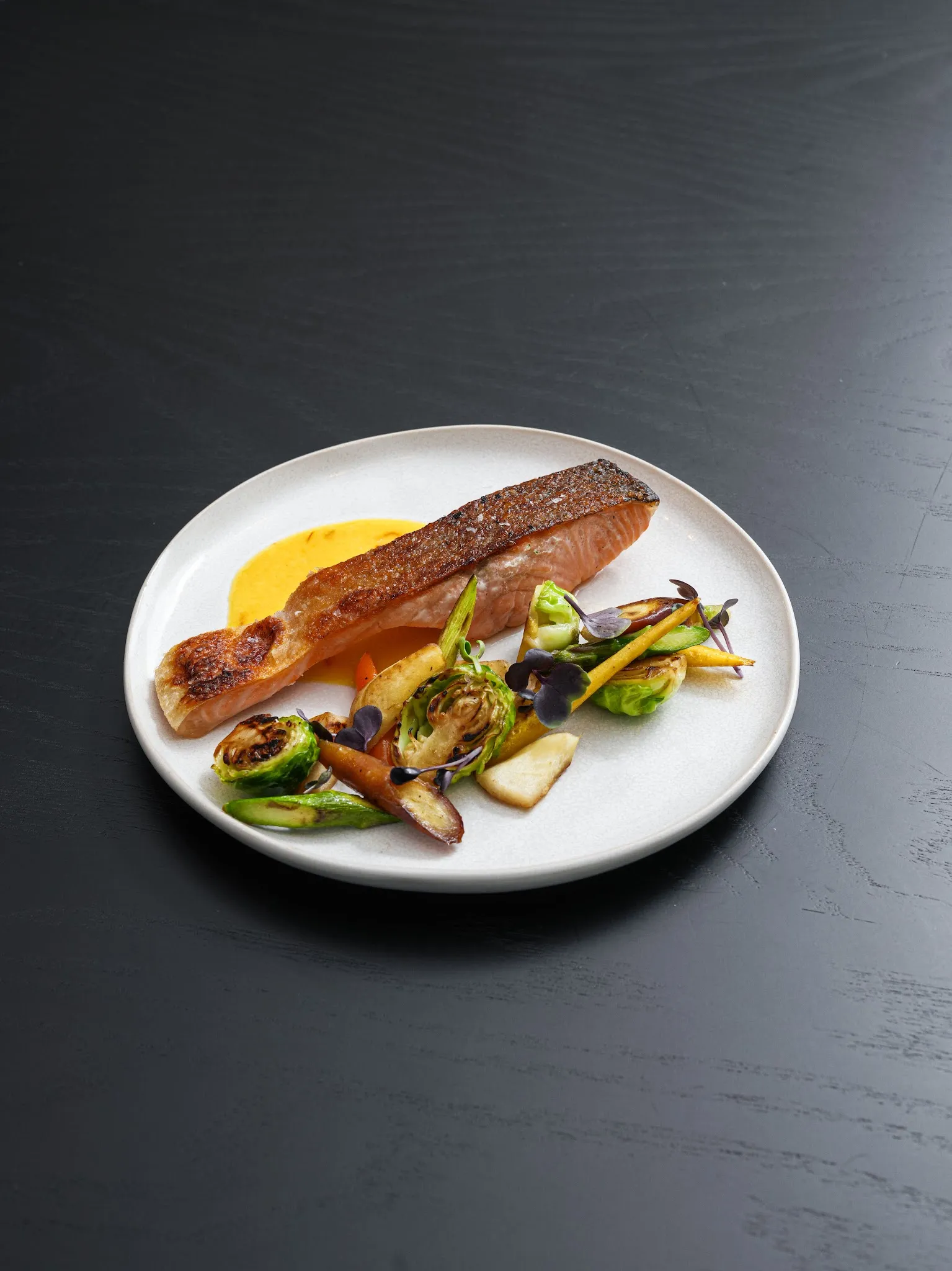 Crispy skinned salmon with charred brussels sprouts and orange sauce on a white plate