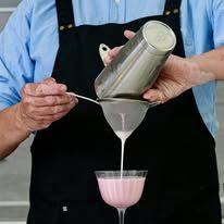 Bartender straining a pink cocktail into a coupe glass using a fine mesh strainer