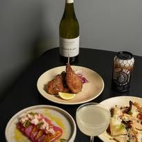 Una Una dinner spread with fried chicken, pink marinated dish, white wine and craft beer