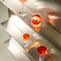 Three cocktails in elegant glassware on a tiered surface, lit with warm golden sunlight